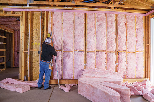 Worker Installing Fiberglass Insulation in Wooden Framed Wall